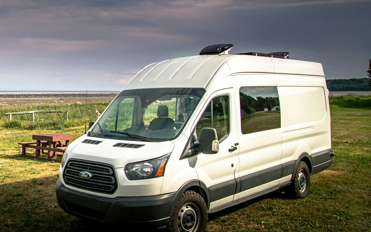 Weißer Ford Transit mit Camper-Ausbau und Dachlüftern im Grünen