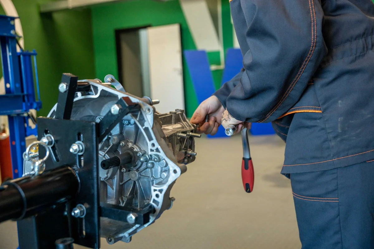 Mechaniker arbeitet am vollständigen ausgebauten Fahrzeuggetriebe auf einem Werkstattständer